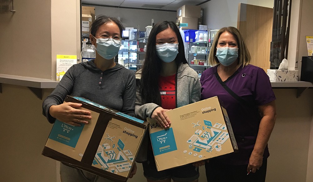 Two women holding each one a box next to a woman dressed as a nurse.
