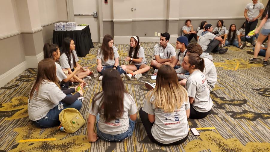 A group of Linens N Love volunteers sit on the floor in a circle talking about their changemaking journeys.