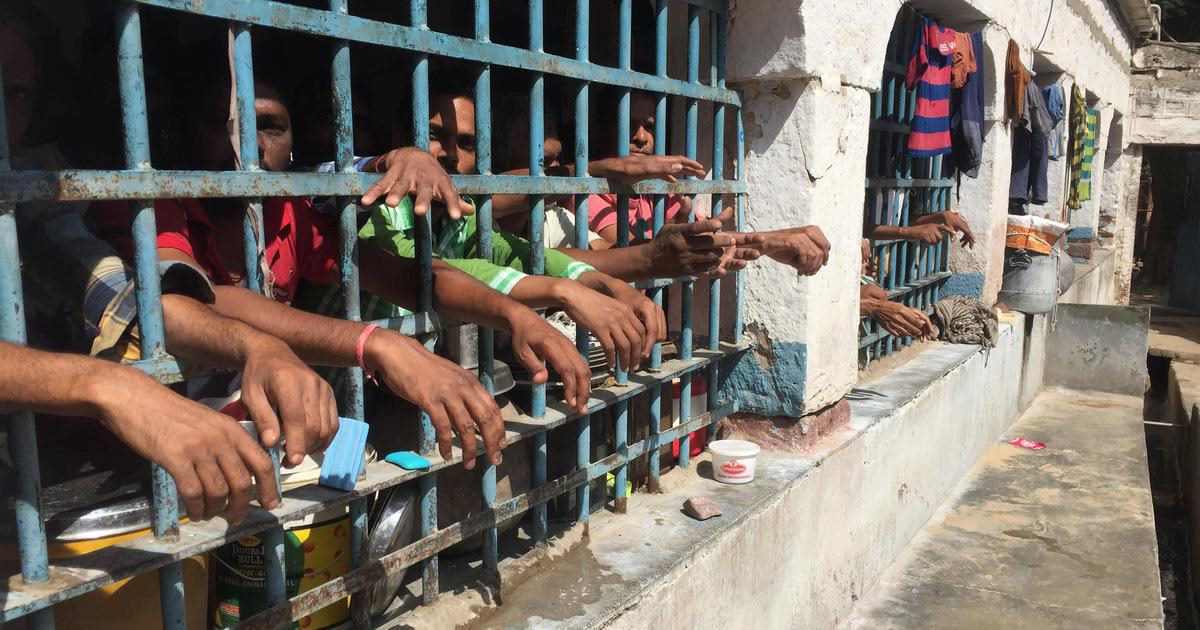 A picture with people behind the fence of a prison.  