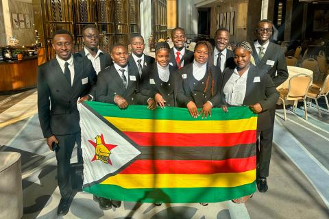 A group of African students dressed in uniform holding a Zimbabwe flag.