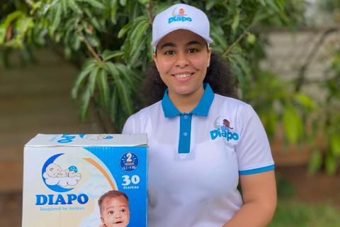 A young woman stands in holding a box of "DIAPO" brand diapers. She's wearing a "DIAPO" branded baseball cap and branded white polo shirt.