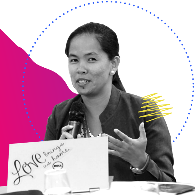 A woman of southeast asian decent holds a microphone, giving a speech. In front of her is a portion of a podium with a laptop.