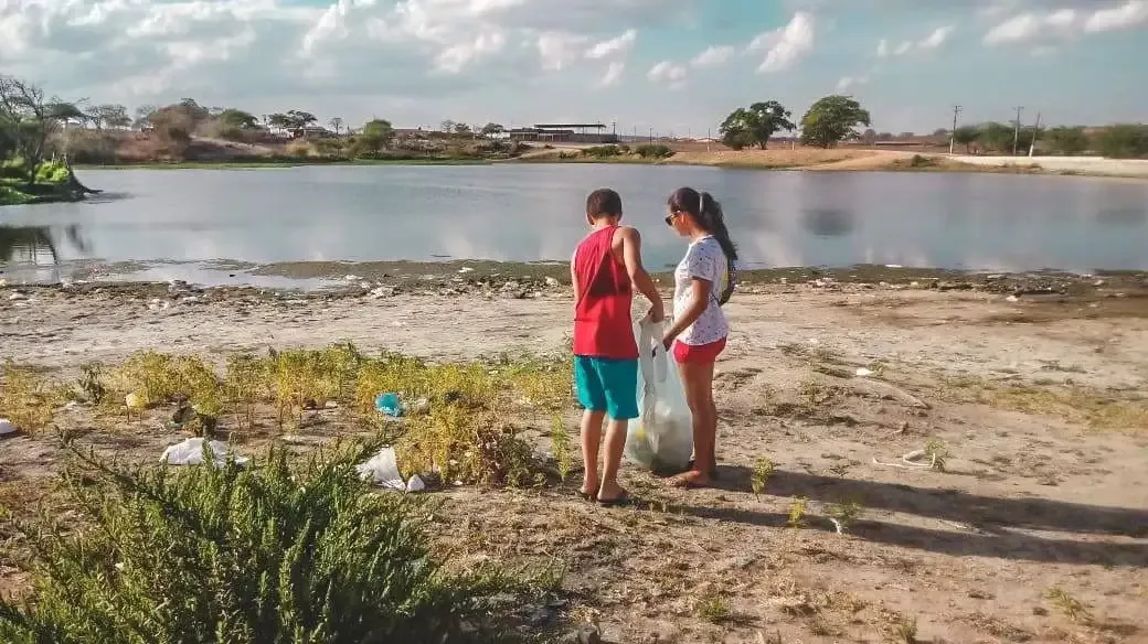 Two young people part of Projeto Arbo cleaning the surroundings of a lake.